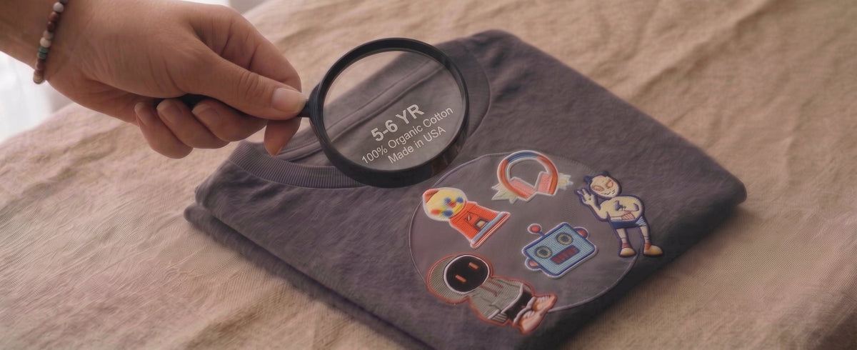 Hand holding a magnifying glass over a children's clothing fabric content tag