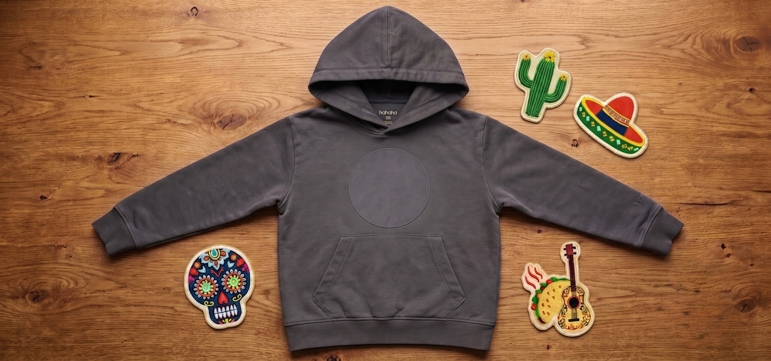 Black organic cotton kids hoodie with a patch area, surrounded by three swappable embroidered patches on a wood surface