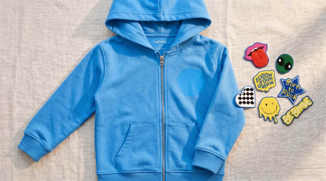 Soft organic cotton kids hoodie laid flat next to interchangeable hook-and-loop patches on a warm wooden surface