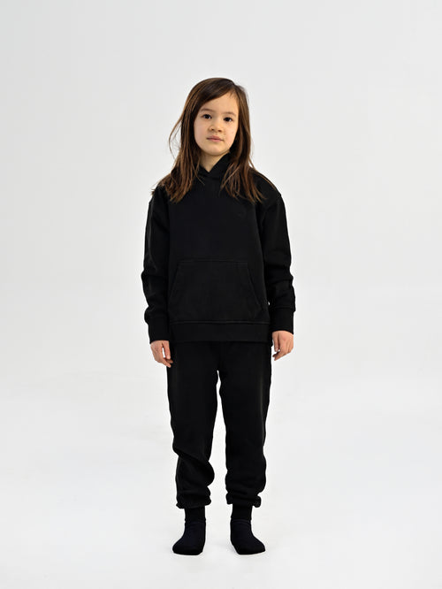 Child wearing black Hahaha organic cotton hoodie with joggers, front view, made in Los Angeles